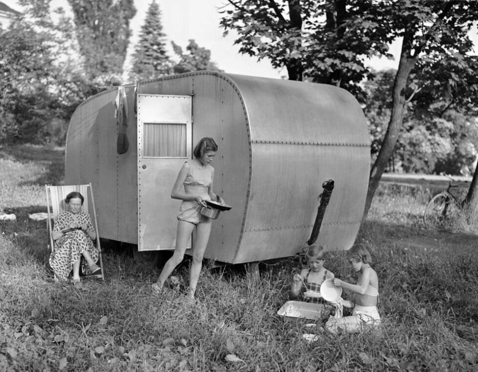 Camping på Huk i 1953. Her en glad familie på fem medlemmer, mor, far og tre jenter, som ferierer i en campingvogn. Middagen er unnagjort, og jentene tar oppvasken ute i det fri, mens mor strikker i fluktstolen. Camping på Huk i 1953. Her en glad familie på fem medlemmer, mor, far og tre jenter, som ferierer i en campingvogn. Middagen er unnagjort, og jentene tar oppvasken ute i det fri, mens mor strikker i fluktstolen. Foto: Jan Stage / NTB / Scanpix
