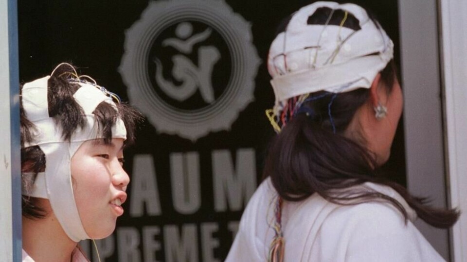 På dette arkivbildet fra 9. mai 1995 ser to kvinnelige tilhengere av dommedagssekten Aum Shinrikyo på en gruppe politifolk som gjennomsøker bygningen deres i Fujinomiya, sentralt i Japan. På dette arkivbildet fra 9. mai 1995 ser to kvinnelige tilhengere av dommedagssekten Aum Shinrikyo på en gruppe politifolk som gjennomsøker bygningen deres i Fujinomiya, sentralt i Japan. Foto: Sadayuki Mikami / AP Photo / NTB