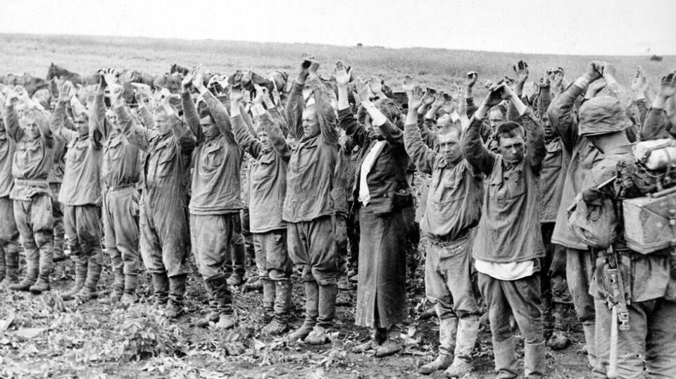Østfronten, desember 1941. Sovjet-russiske krigsfanger står med armene i været et ukjent sted. En tysk soldat helt til høyre i bildet. Foto: NTB scanpix/ Tysk kilde