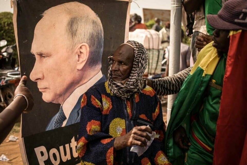 En mann i Mali sitter foran et bilde av den russiske presidenten Vladimir Putin. Russiske soldater har erstattet franske som leverandør av sikkerhetstjenester.