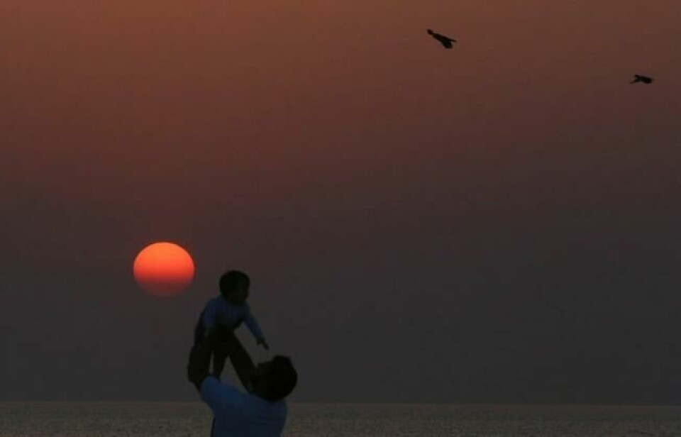 En mann holder opp et spedbarn ved solnedgang på stranden i Kuwait City den siste dagen av den religiøse høytiden Eid al-Fitr, 8. juni 2019. NTB Scanpix/AFP. En mann holder opp et spedbarn ved solnedgang på stranden i Kuwait City den siste dagen av den religiøse høytiden Eid al-Fitr, 8. juni 2019. NTB Scanpix/AFP.