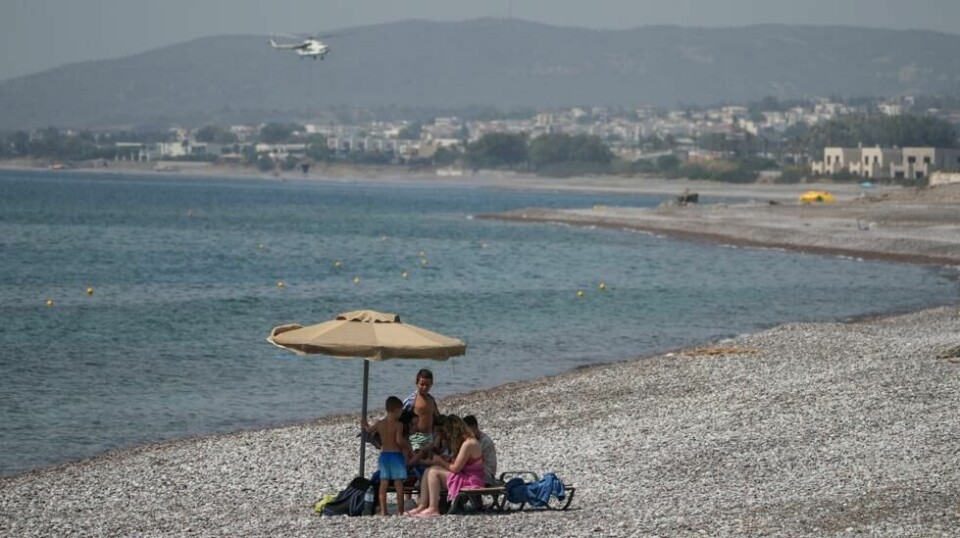 Turister på en strand på Rhodos i fjor sommer. I bakgrunnen et brannhelikopter.