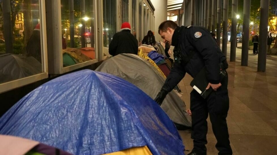 En politimann sjekker innom et telt i en migrantleir i Paris tirsdag morgen. Foto: Nicolas Garriga / AP / NTB