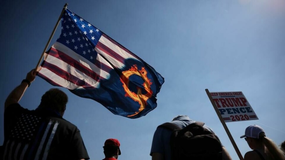 Symbolet «Q» er flittig brukt for å vise sin støtte og tilhørighet til bevegelsen QAnon. Her holder en Trump-tilhenger opp et amerikansk flagg med en brennende Q på under et valgmøte i Portland i delstaten Oregon.