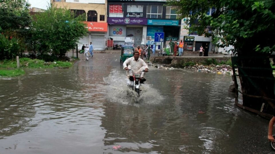 Tolv mennesker døde i et jordskred i det nordvestlige Pakistan natt til fredag. Skredet ble utløst av kraftig regn. Her kjører en motorsyklist gjennom en oversvømmet gate i Peshawar i slutten av juli. Foto: Muhammad Sajjad / AP / NTB