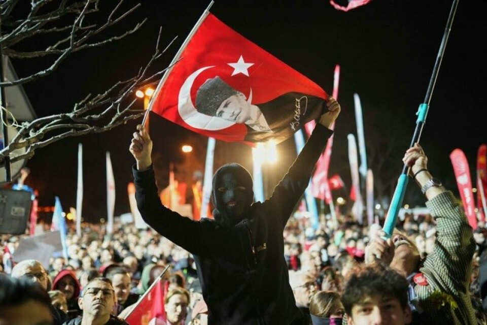 En maskert demonstranter holder opp et tyrkisk flagg med bilde av landsfaderen Mustafa Kemal Atatürk, som grunnla den moderne tyrkiske staten for drøyt 100 år siden.