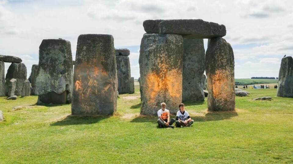 To aktivister fra gruppa Just Stop Oil sitter foran Stonehenge-formasjonen etter å ha sprayet noe som ligner oransje maling på den. Foto: Just Stop Oil / AP / NTB