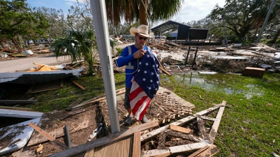 Chris Jordan heiser et amerikansk flagg over ruinene av rådhuset i Horseshoe Beach i Florida lørdag. Foto: Gerald Herbert / AP / NTB