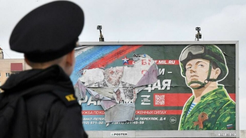 En russisk militærkadett står foran en reklametavle som reklamerer for militærtjeneste i Sankt Petersburg. Illustrasjonsfoto.