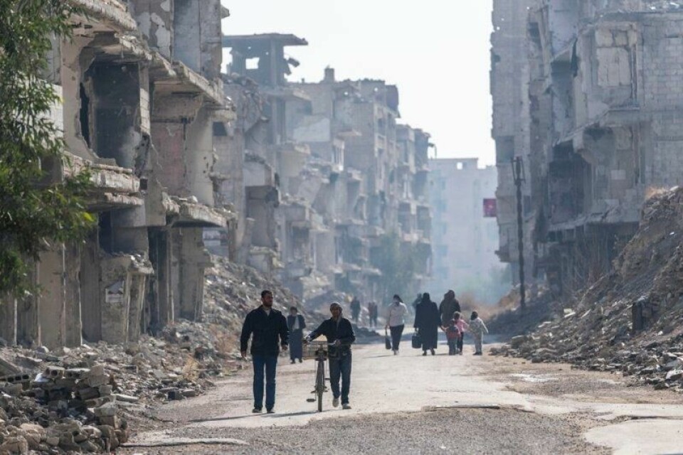 Folk vandrer i gater med ødelagte bygninger etter krigen i Syria i en leir for palestinske flyktninger i Damaskus i Syria i januar i år.