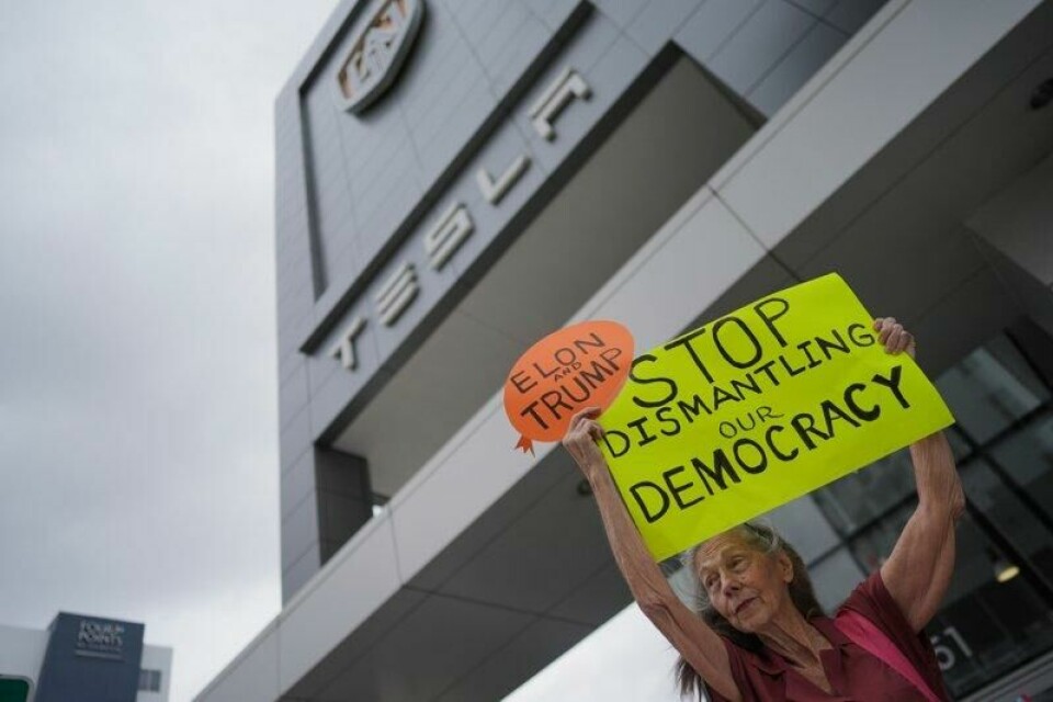 En demonstrant holder opp en plakat med teksten «Stans nedbrytingen av demokratiet» utenfor en Tesla-forhandler i Miami lørdag.
