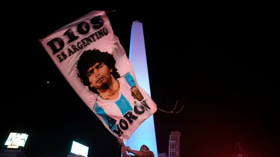 En mann vaier et flagg med bildet av Diego Maradona i sentrum av Buenos Aires i timene etter fotballegendens bortgang. Foto: Victor Caivano / AP / NTB