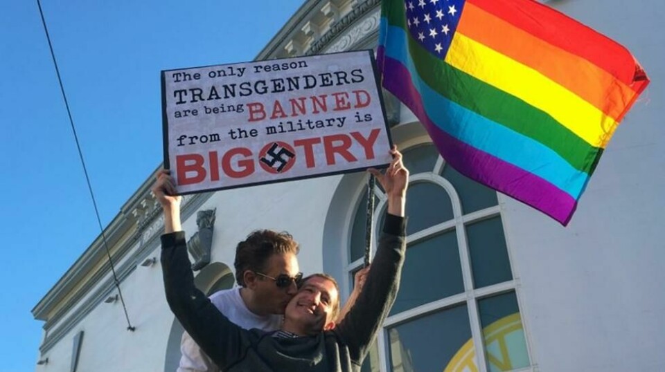 San Francisco-paret Nick Rondoletto og Doug Thorogood vifter med et regnbueflagg og holder opp en plakat for å protestere mot et foreslått forbud mot transpersoner i militæret, under en protestaksjon i 2017. Den gang havnet Donald Trumps forsøk på å stenge transpersoner ute fra militæret i rettssystemet i flere år. Nå har en dommer blokkert et nytt forsøk fra presidenten.