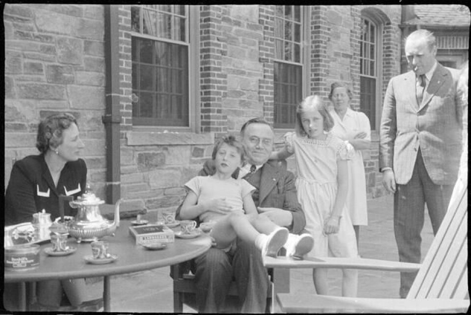 USA, 9. mai 1942. Statsminister Johan Nygaardsvold med prins Harald på fanget. Til høyre står prinsesse Ragnhild. Kronprins Olav og kronprinsesse Märtha i hver sin ytterkant av bildet. I bakgrunnen ses Signe Svendsen, prins Haralds barnepike. USA, 9. mai 1942. Statsminister Johan Nygaardsvold med prins Harald på fanget. Til høyre står prinsesse Ragnhild. Kronprins Olav og kronprinsesse Märtha i hver sin ytterkant av bildet. I bakgrunnen ses Signe Svendsen, prins Haralds barnepike. Foto: Nikolai Ramm Østgaard / Riksarkivet