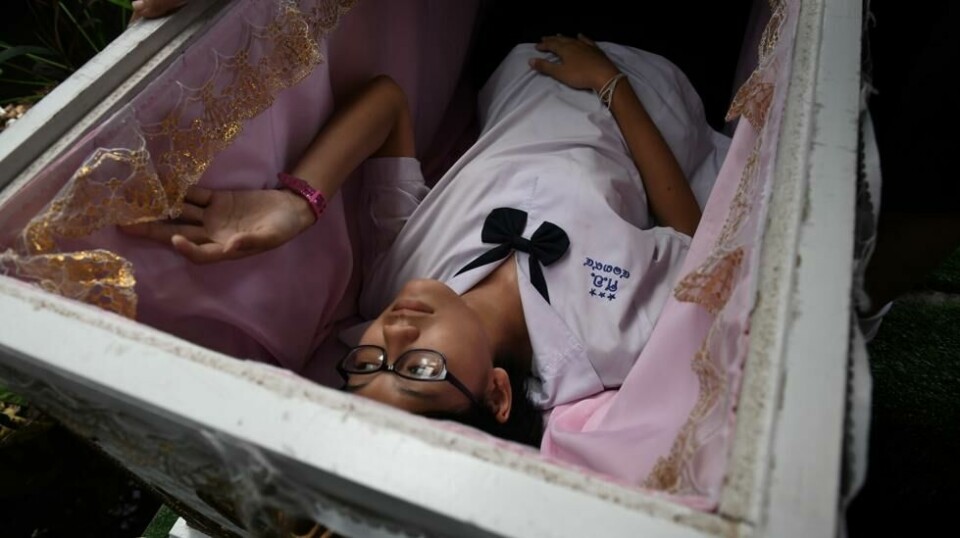 En tenåringsjente prøver ut en tradisjonell thailandsk begravelseskiste på Kid Mai Death Awareness Cafe. Foto: AFP
