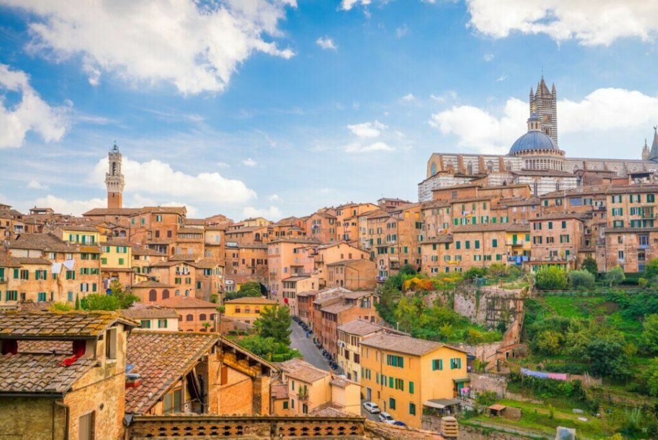 Siena i Toscana, Italia, tar deg med tilbake i tid når du vandrer gjennom de små, sjarmerende gatene. (Foto: Colourbox) Bilde av den pittoreske byen Siena, Toscana i Italia på en solrik dag med blå himmel og noen skyer. Byen er bygget på en ås, og de historiske bygningene er tett sammen med karakteristiske røde tak og varme jordfarger. Øverst i bildet kan man se den imponerende katedralen i Siena med sin kuppel og gotiske detaljer. Flere grønne områder og hager kan ses mellom bygningene, noe som gir byen et frodig utseende. Vi har laget en omfattende guide til Toscana i Italia hvor vi blant annet forteller om fem populære byer som Firenze, Pisa, Siena, Montepulciano og Volterra. Vi gir deg også forslag til tre kjøreruter du kan ta for å oppleve vingårder og resten av Toscana. La deg inspirere av den italienske regionen som fikk sitt eget TV-program; «Den store matfesten - Toscana»