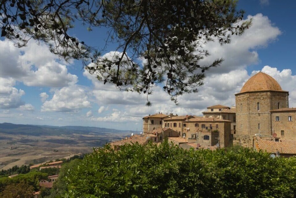 Volterra er en populær by i Toscana, Italia, som byr på fantastisk utsikt over regionen med de mange vingårdene. (Foto: Colourbox) Bilde av byen Volterra i Toscana, Italia, på en dag med blå himmel og spredte skyer. Byen har historiske bygninger med røde tak, inkludert en stor rund kuppel til høyre i bildet. I forgrunnen er det frodige trær som rammer inn scenen, og utsikten strekker seg utover det bølgende toskanske landskapet med åser og daler i bakgrunnen. Vi har laget en omfattende guide til Toscana i Italia hvor vi blant annet forteller om fem populære byer som Firenze, Pisa, Siena, Montepulciano og Volterra. Vi gir deg også forslag til tre kjøreruter du kan ta for å oppleve vingårder og resten av Toscana. La deg inspirere av den italienske regionen som fikk sitt eget TV-program; «Den store matfesten - Toscana»