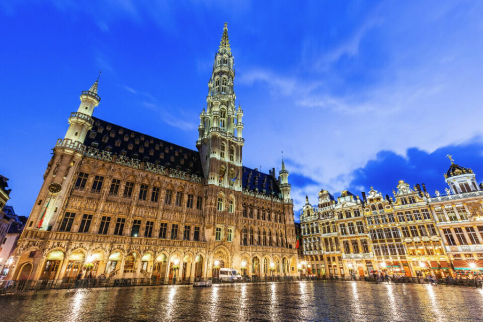 Grand Place (Grote Markt) i Brussel er kjent for sin fantastiske arkitektur og regnes som en av de vakreste torgene i Europa. Den mest fremtredende bygningen i bildet er Brussel rådhus. (Foto: Canva) Dette bildet viser Grand Place (Grote Markt) i Brussel, Belgia, ved skumring eller kveld. Plassen er kjent for sin fantastiske arkitektur og er en av de vakreste torgene i Europa. Den mest fremtredende bygningen i bildet er Brussel rådhus (Hôtel de Ville), en gotisk bygning med et høyt, detaljert tårn og en fasade dekorert med statuer. Til høyre i bildet ser vi overdådig dekorerte gildehus, som tilhørte ulike laug og handelsmenn i byen. Lyset fra bygningene reflekteres vakkert på den brosteinsbelagte plassen, og den dype blå himmelen gir en dramatisk kontrast til de gyldne detaljene i arkitekturen. Dette er et av UNESCOs verdensarvsteder og et populært reisemål for turister som besøker Brussel.