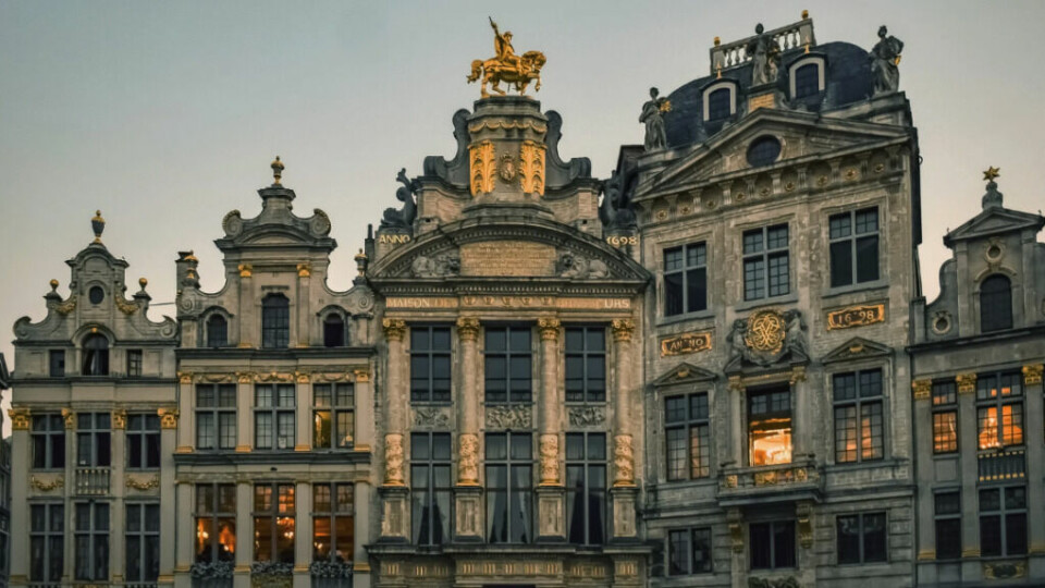 Overdådig dekorerte gildehus fra slutten av 1600-tallet på hovedtorget Grand Place (Grote Markt) i Brussel, Belgia. Bygningen i midten er Maison des Brasseurs (Bryggernes hus), som har en gyllen rytterstatue på toppen. (Foto: Canva) Dette bildet viser en del av Grand Place (Grote Markt) i Brussel, Belgia, en av de mest ikoniske plassene i Europa og et UNESCO-verdensarvsted.Bygningene på bildet er overdådig dekorerte gildehus fra slutten av 1600-tallet, preget av rikt utsmykkede fasader, forgylte detaljer og skulpturer. Den mest fremtredende bygningen i midten er Maison des Brasseurs (Bryggernes hus), som har en gyllen rytterstatue på toppen. Tallene «1698» på fasaden markerer året bygningen ble rekonstruert etter at mye av plassen ble ødelagt i 1695.Belysningen gir en varm glød fra vinduene, noe som skaper en stemningsfull kontrast mot de mørkere steindetaljene. Bildet fanger den tidløse elegansen og den historiske sjarmen som gjør Grand Place til et av de mest populære reisemålene i Brussel.Overdådig dekorerte gildehus fra slutten av 1600-tallet på hovedtorget Grand Place (Grote Markt) i Brussel, Belgia. Bygningen i midten er Maison des Brasseurs (Bryggernes hus), som har en gyllen rytterstatue på toppen.