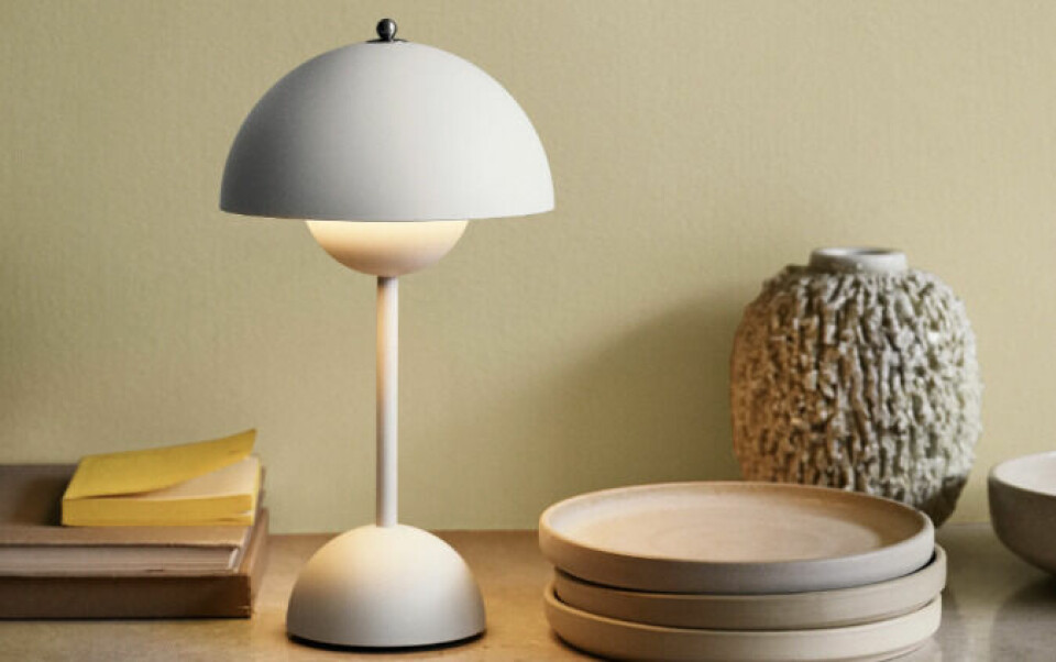 Flowerpot VP3 er en oppladbar bordlampe uten ledning som enkelt kan flyttes rundt. (Foto: Nordic Nest) Flowerpot portable hvit bordlampe VP9, på skjenk med tallerkner og annet interiør, mot en beige vegg. Flowerpot lampe: En dansk klassiker av Verner Panton.