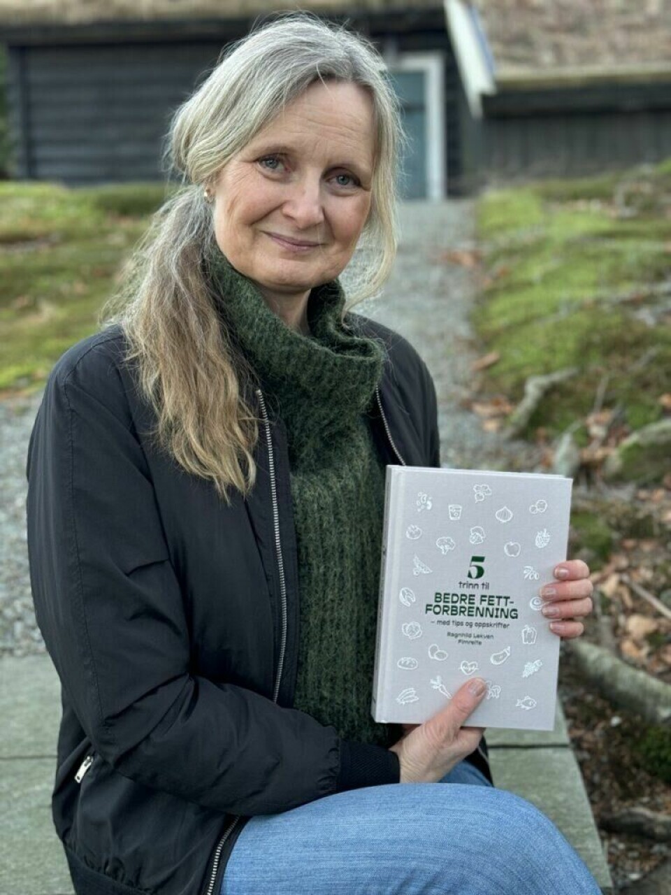 Klinisk ernæringsfysiolog Ragnhild Lekven Fimreite deler sin beste frokost for en god start på dagen. Bilde av ernæringsfysiolog Ragnhild Lekven Fimreite. Forfatteren av boken 5 trinn til bedre fettforbrenning som sitter smilende med boken sin i handen ute i naturen med trehus i bakgrunnen. Vi har fått oppskrift på sunn, hjemmelaget granola som passer perfekt til yoghurt av Ragnhild!