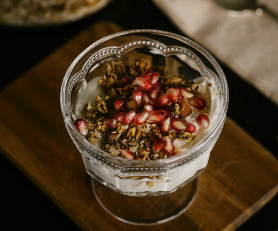 Det er lite som er så godt til frokost eller kvelds som en knasende sprø granola eller müsli, med bær, yoghurt melk eller honning! Hvordan du spiser den velger du selv, men her har du oppskrift på en hjemmelaget, enkel og smakfull ovnsbakt granola som attpåtil er sunn! (Foto: Ragnhild Lekven Fimreite) Bildet viser en glasskål med hjemmelaget granola. Skålen er fylt med en blanding av hvit yoghurt og sprø granola, og på toppen er det drysset med røde granateplekjerner. Granolaen ser ut til å inneholde ulike nøtter og frø, og det er en rustikk treplate under skålen. Bakgrunnen er noe uskarp, men det ser ut til å være en lys serviett eller klut i nærheten. Den delikate presentasjonen gir inntrykk av en sunn og appetittvekkende frokost eller snack. Vi har fått oppskrift på granola, en form for hjemmelaget og sunn ovnsbakt müsli av ernæringsfysiolog Ragnhild Lekven Fimreite. Forfatteren av boken 5 trinn til bedre fettforbrenning.