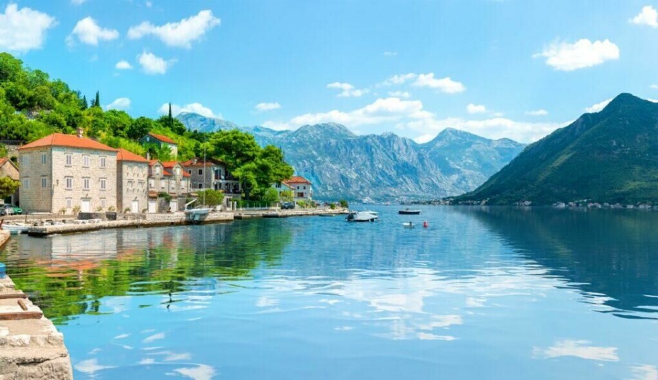 Montenegro er virkelig en skjult skatt i Adriaterhavet som bør utforskes. Her får du vakre landsbyer, som Kotor, spennende historie og behagelige temperaturer. Og ikke nok med det, Montenegro er også billig å feriere i. (Foto: Colourbox) Bildet viser byen Kotor i Montenegro. Landsbyen består av gamle steinhus med røde tak som ligger tett i tett langs en rolig havnefront. Små båter flyter på det speilblanke vannet, som reflekterer en klar blå himmel og de omkringliggende grønne åsene. Bakgrunnen domineres av dramatiske fjelltopper som skaper en imponerende og vakker naturskjønn ramme rundt denne sjarmerende kystlinjen. Vi hjelper deg med å finne billig ferie, og svarer på spørsmål som hvor er det billig å reise, hva koster en halvliter øl, og avslører fem land som er kåret til de billigste i Europa for nordmenn å feriere i.