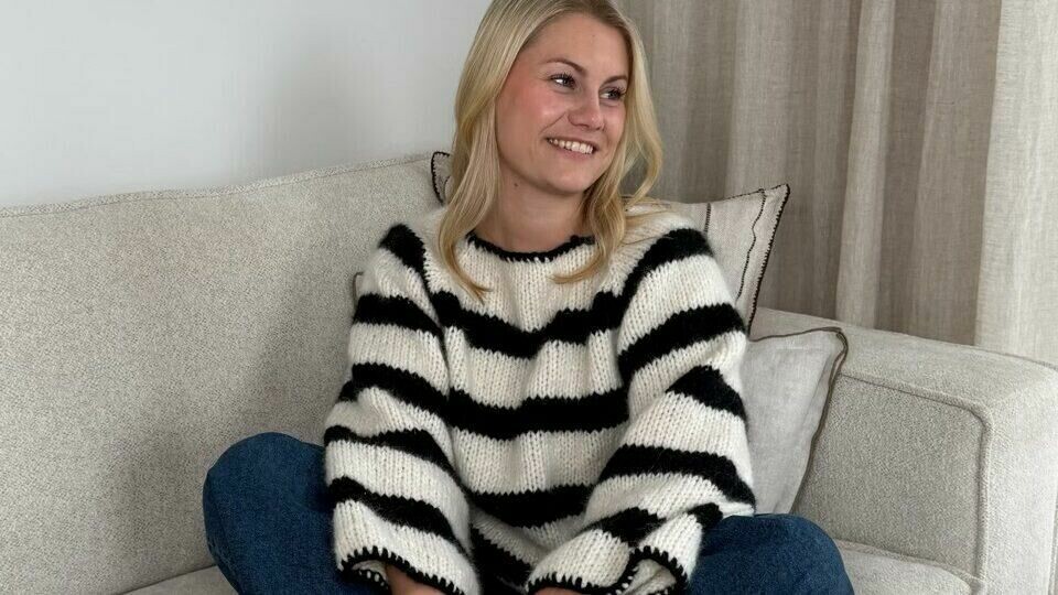 Klassiske striper og myk raglanstrikk – Emilie viser frem Fridagenseren, en must-have i enhver garderobe. (Foto: Knitting by Emilie) Emilie sitter avslappet på en lys sofa iført sin egen strikkegensermodell, Fridagenseren fra Knitting by Emilie. Genseren har et tidløst design med brede sorte og hvite striper, perfekt for en stilren og komfortabel hverdagslook. Hun kombinerer den med vide denimjeans og svarte sokker, mens hennes røde neglelakk tilfører en elegant kontrast. Bakgrunnen består av beige gardiner og en minimalistisk interiørstil, som fremhever den lune og avslappede stemningen.