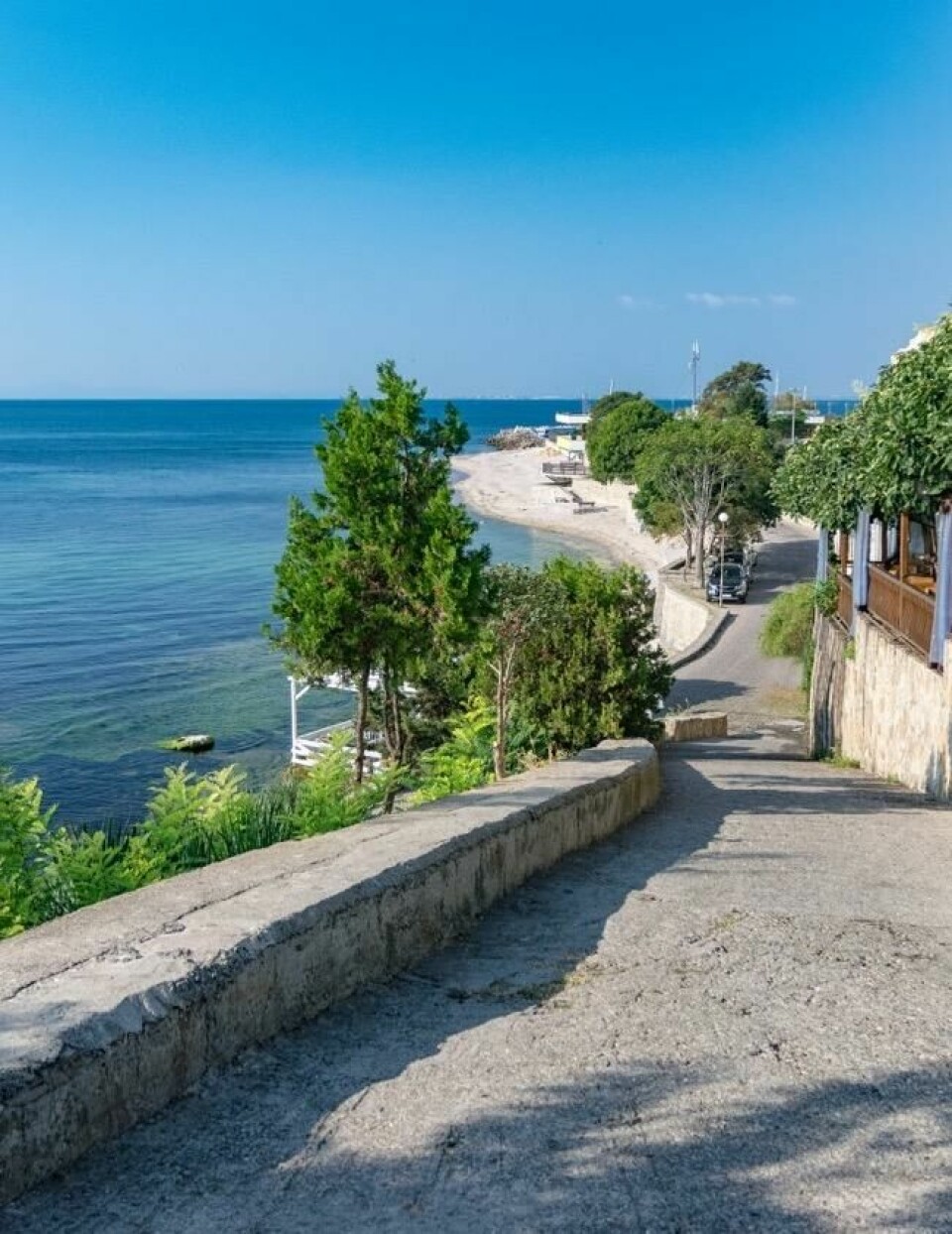 Nessebar er en sjarmerende by som bør oppleves dersom man reiser til Bulgaria. Vi hjelper deg å finne billige reiser til landet. Bilde av en gate i Nessebar hvor du ser havet på venstre side og noen hus på høyre side, og en strand i bakgrunnen. Her finner du billige reiser til Bulgaria til populære destinasjoner langs kysten som Nessebar og Sunny Beach.