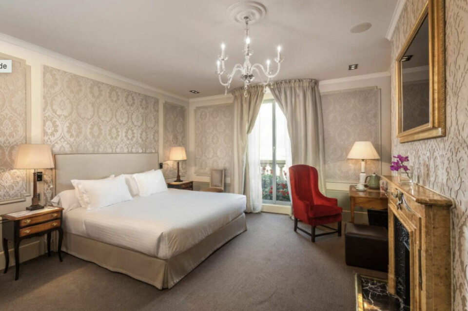 Rommene på Hotel El Palace er like elegant innredet som resten av hotellet. Hotellrom i Barcelona med dobbeltseng og rød lenestol og peis i gull.
