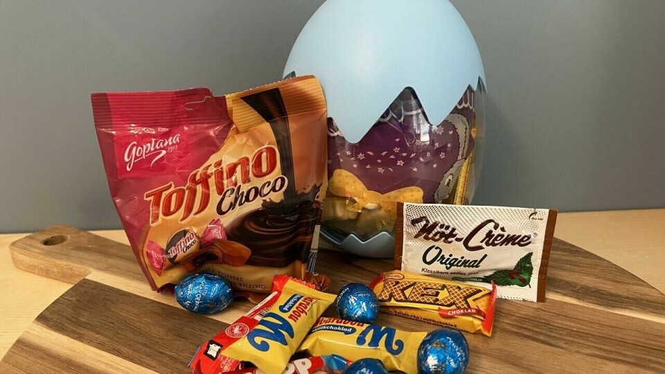 Egg-stravaganza påskeegg med et variert utvalg av sjokolade og karameller, inkludert Plopp, Kex og Toffino Choco – perfekt for en søt påskekos! (Foto: Ole Kristian Aaknes) På bildet ser vi et Egg-stravaganza påskeegg, som skiller seg ut med sin halvtransparente plastdesign. Den øvre halvdelen av egget er lyseblå med en tagget kant, som gir inntrykk av et egg som har sprukket. Gjennom plasten kan vi se godteriet inni, blant annet en stor pose påskeskum.Foran egget ligger et variert utvalg av påskegodteri, inkludert en pose Toffino Choco (sjokoladefylte karameller), en pakke Nöt-Crème Original, samt kjente sjokoladebiter som Plopp, Kex, Marabou M og sjokoladeegg i blå folie. Godteriet er plassert på et rundt trefat, og bakgrunnen er en nøytral blågrå vegg.