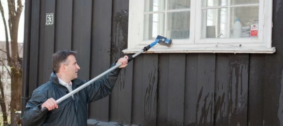 Med kost og forlengerskaft kan du vaske huset en dag det er overskyet eller regnvær. Mann som vasker brunt hus med kost og forlengerskaft til husvask.