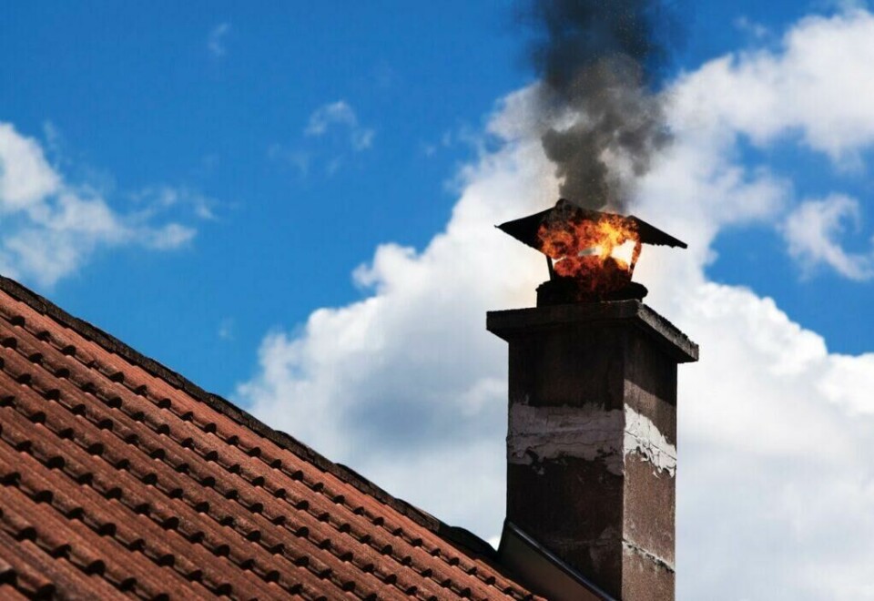 Å unngå å fyre med papir og papp er derfor en enkel og viktig måte å redusere risikoen for pipebrann. (Foto: Colourbox) Bilde av pipe med brann på rødt tak og med blå himmel i bakgrunn.