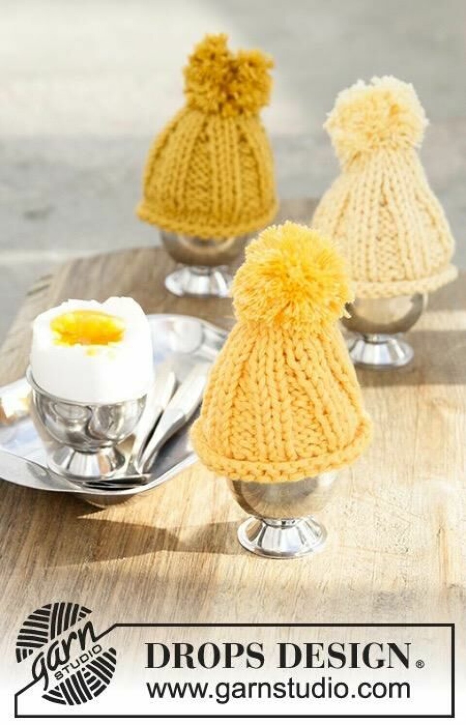 Vi har samlet strikkepakker og gratis strikkeoppskrifter som er perfekte som påskestrikk. Tre egglass i sølv med små gule luer med dusk som holder egget varmt. Ved siden av står et egg med toppen kuttet av. Her finner du strikkepakker til dame og barn, samt gratis strikkeoppskrifter for nybegynnere og viderekommende.