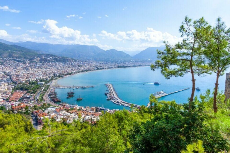Alanya i Tyrkia er populært blant reisende som søker strandferie kombinert med spennende nattliv. (Foto: Colourbox) Utsiktsbilde over Alanya i Tyrkia. I forgrunnen ser du grønne busker og trær, mens i bakgrunnen ser du en gyllen strand, molo, blått hav og en rekke murhus med røde tak. Vi hjelper deg med å finne den beste reisen til Tyrkia for deg ved å fortelle om hva du kan gjøre i blant annet Antalya, Side og Alanya.