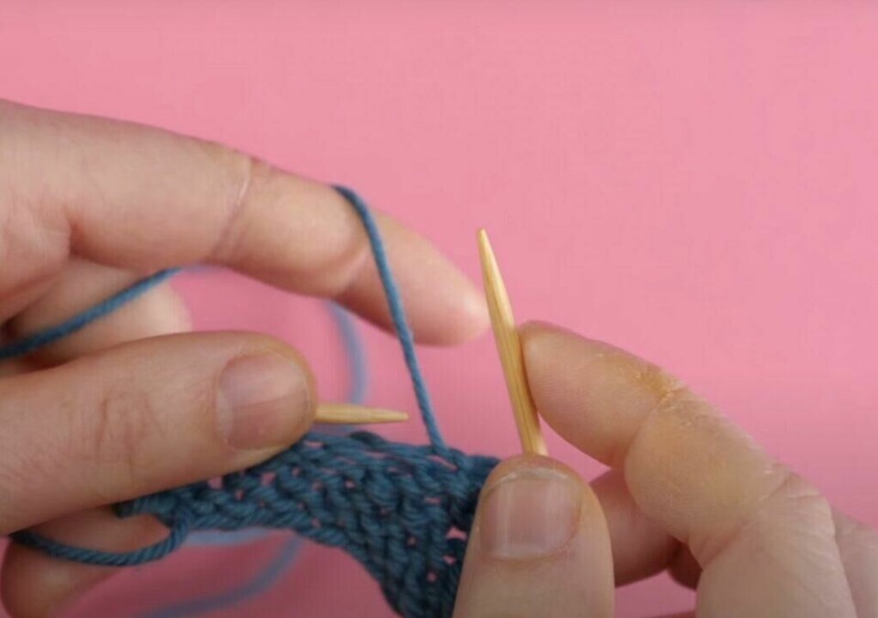 5) Ferdig! Nå har du strikket din første maske vrang. (Foto: ABC Brand Studio) Bilde av hvordan strikke vrang med blått garn, strikkepinner i tre og rosa bakgrunn