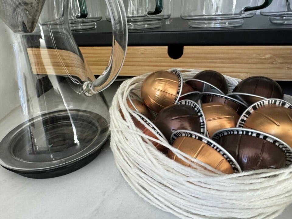 Hjemmelaget bolle i hvitt garn, perfekt for oppbevaring av kaffekapsler eller andre små ting. (Foto: Kreative Ideer/ Aurora Lange) En bolle laget av hvitt garn er fylt med fargerike kaffekapsler i metalliske toner. Bollen står ved siden av en moderne glasskanne på en lys benkeplate, og gir et stilfullt og kreativt uttrykk i kjøkkeninnredningen.