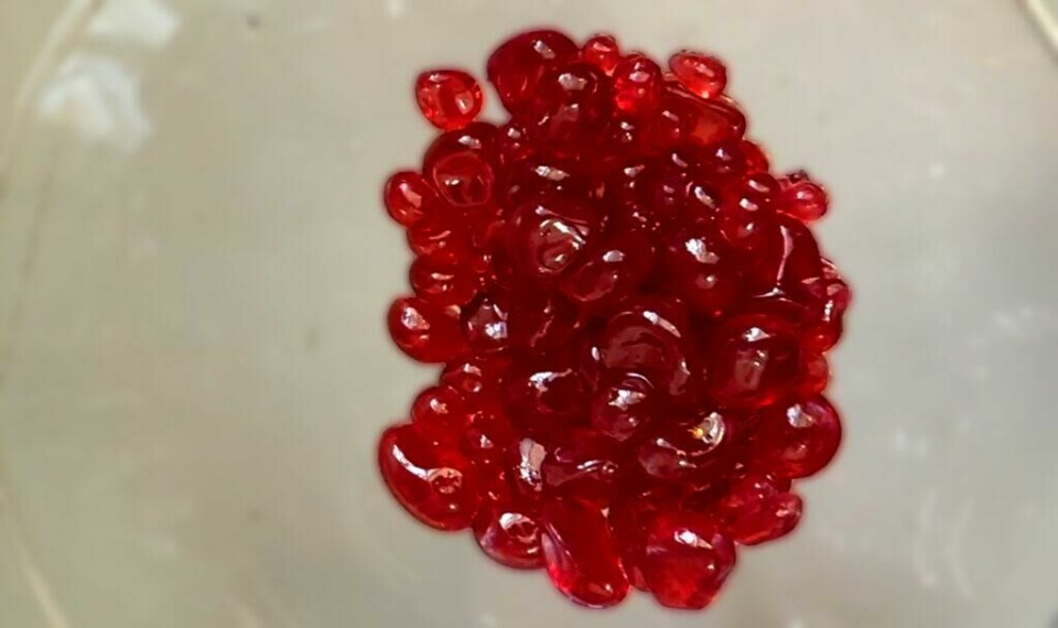 Fruktkaviar, fruktbobler og fruktperler - kjært barn har mange navn. (Foto: Kreative Ideer/ Miriam Schjetlein) Røde fruktperler på grå bakgrunn.