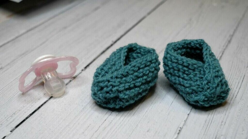 Babysokkene er en ypperlig barselgave - og strikkes kjapt med bare rette masker. (Foto: Kreative Ideer/ Miriam Schjetlein) To strikkede babysokker i sjøgrønn farge. Smokk som ligger ved siden av. Gratis strikkeoppskrift på søte babytøfler