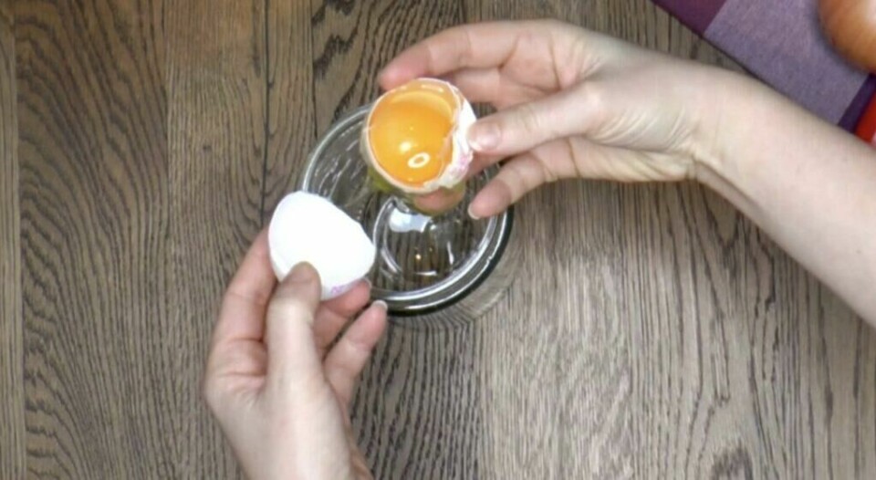Tradisjonell teknikk der egget vippes mellom skallhalvdelene. (Foto: Kreative Ideer) To hender holder hver sin halvdel av et knekt egg over en liten glassbolle. Eggeplommen beveges forsiktig mellom skallhalvdelene mens eggehviten drypper ned. Dette er en klassisk metode som gir god kontroll når man skiller egg for hånd.