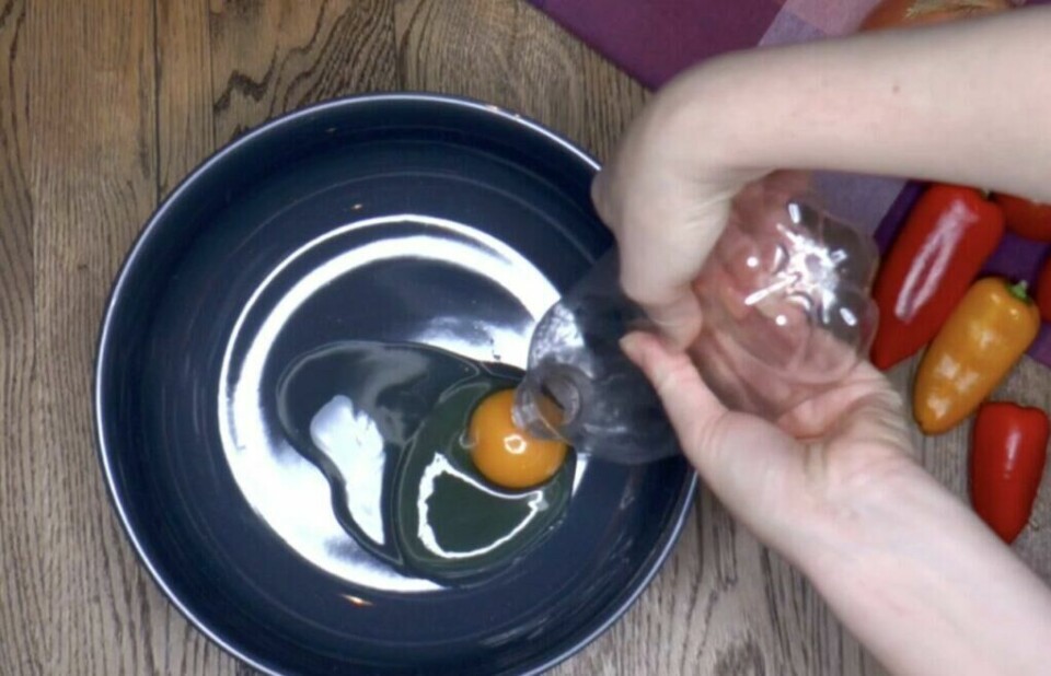 Med en plastflaske kan du raskt trekke opp eggeplommen. (Foto: Miriam Schjetlein) En hånd klemmer på en tom plastflaske og bruker den til å suge opp eggeplommen fra en mørk bolle. Egget er allerede knekt, og eggeplommen trekkes inn i flasken mens eggehviten blir igjen. Dette er en kreativ og rask metode som krever minimalt med utstyr.