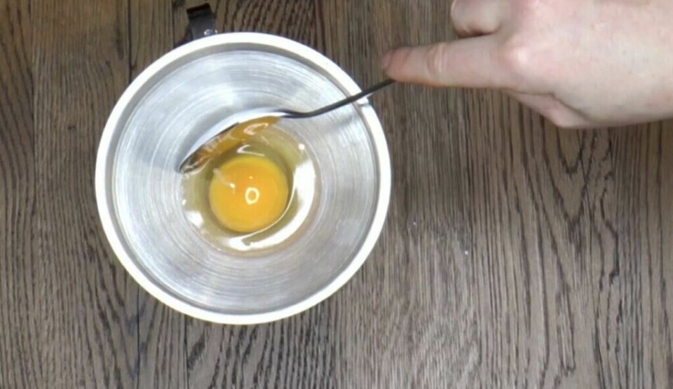 Trakt gir en enkel måte å skille eggehvite fra plomme på. (Foto: Miriam Schjetlein) Et egg er knekt i en metalltrakt som står i en bolle på et mørkt tremønstret underlag. En hånd holder i trakten mens eggehviten har rent gjennom, og eggeplommen ligger igjen øverst. Dette viser en praktisk metode for å skille egg ved hjelp av trakt, der plommen blir igjen og hviten siles ned.