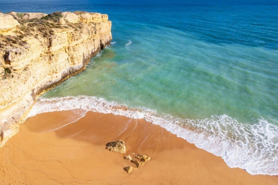 Albufeira er en populær destinasjon for deg som drømmer om å reise til Algarvekysten i Portugal. (Foto: Colourbox) Bildet viser en vakker strand i Albufeira langs Algarve-kysten i Portugal. Stranden består av gyllen sand med noen få spredte steiner, og ligger ved foten av høye, klippeformasjoner av lyse steiner. Bølgene skvulper forsiktig inn mot kysten fra det klare, blågrønne vannet. Havet strekker seg ut i horisonten under en klar, blå himmel, og gir et fredelig og innbydende inntrykk. Vi hjelper deg med å planlegge ferien til Algarve-kysten i Portugal. Vi gir deg alt fra tips til byer; Lagos, Faro, Tavira, Albufeira og Sagres. Samt hvor du kan finne hotell langs Algarve-kysten og shoppingmulighetene.