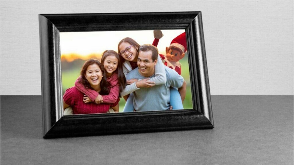 Rampenissen slår til igjen med en uventet fotobombe i familiebildet! (Foto: Kreative Ideer/ Miriam Schjetlein) Bildet viser en innrammet familiefotografi hvor en familie på fire smilende poserer utendørs. Alle ser glade og avslappede ut, og solen ser ut til å være på vei ned i bakgrunnen, noe som gir et varmt lys til bildet. Men, i hjørnet av bildet ser vi Rampenissen som har 'fotobombet' bildet ved å snike seg inn i rammen med et lekent uttrykk. Rampenissen er kjent for sine rampestreker, og denne gangen har den bestemt seg for å bli med i familiebildet på en humoristisk måte. Dette gir bildet en morsom og uventet vri.