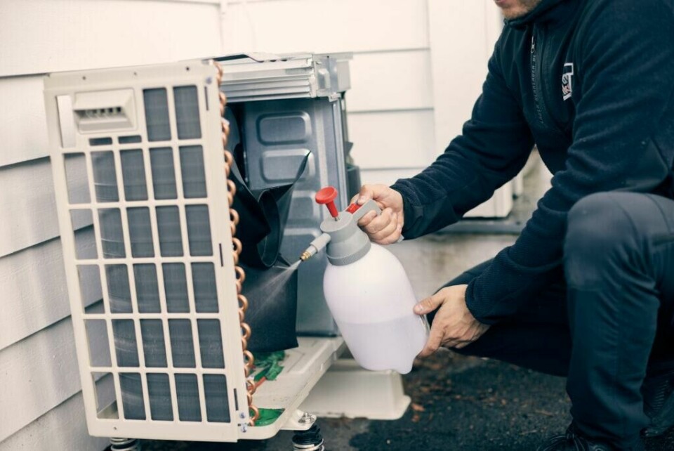 Utedelen trenger også grundig rengjøring for å sikre at varmepumpen fungerer best mulig. (Foto: Varmepumpekjeden Enkon) Bilde av en installatør som har service på varmepumpe, utedelen som henger lavt nede på husveggen. Vi har snakket med eksperten som forteller alt du må vite om service på varmepumper, uavhengig av om du har luft til luft-varmepumpe fra Mitsubishi, Toshiba, Daikin eller Panasonic.