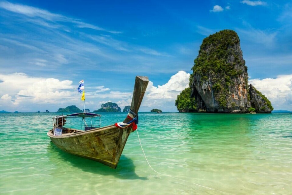 Krabi er et populært reisemål i Thailand, og her får du krystallklart vann, hvite strender og spektakulære kalkesteinsklipper. Perfekt for en eventyrlig ferieopplevelse. (Foto: Colourbox) En tradisjonell thailandsk longtail-båt ligger forankret ved en strand med klart, turkis vann. I bakgrunnen sees en majestetisk, grønnkledd kalksteinøy som stiger opp fra havet under en skyfri himmel. Vi hjelper deg med å finne reise til Thailand, enten du vil ha billige reiser med restplasser, eller kanskje pakkereiser til de populære destinasjonene Phuket, Hua Hin og Krabi. Her finner du også hotell i Thailand.