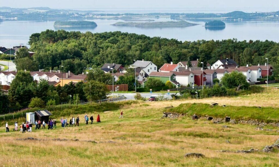 På Flat-Jæren er det registrert nærmere 200 ødegårder fra folkevandringstiden. Jernaldergården er en av dem. (Foto: Torgeir Esig Sørensen / Flickr) Bilde av flat-Jæren hvor Jernaldergården ligger, med hus, folk og gress i front og hav med øyer i bakgrunnen.