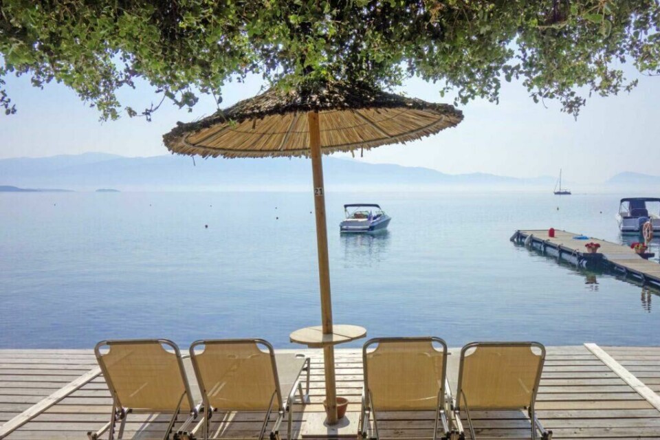 Lefkas er kjent for sine spektakulære strender, her er utsikten fra en av strendene på den greske ferieøya. (Foto: Apollo) Bilde fra sommerferie i syden på greske Lefkas. Solsenger og parasoller med utsikt til havet og båt.
