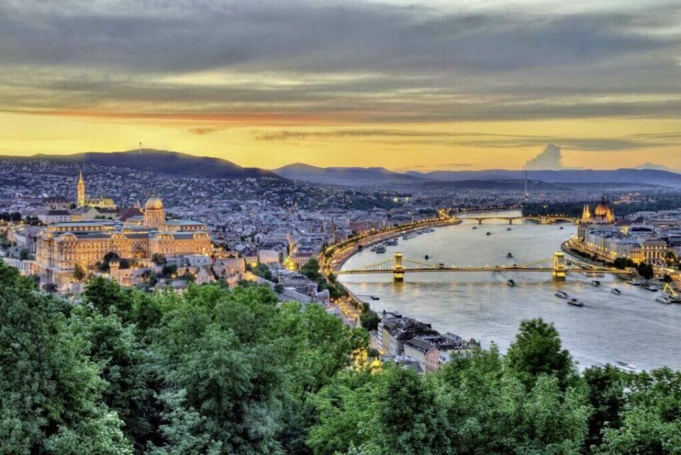 Budapest er en storby flere av oss ikke har besøkt, Hvorfor ikke ta turen i 2025? (Foto: Apollo) Bildet viser en vakker kystlinje med gyldne sandstrender omgitt av lyse kalksteinsklipper. Klippene har naturlige buer og hulrom som skaper et dramatisk landskap. Det turkise vannet slår forsiktig mot stranden, og i bakgrunnen er det grønt landskap som strekker seg mot horisonten under en klar blå himmel.