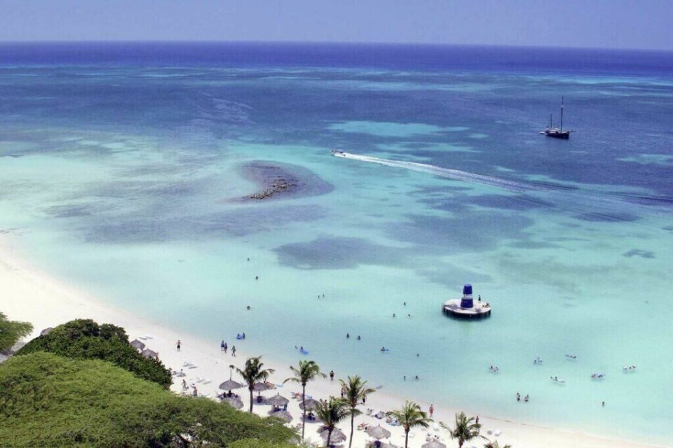 Aruba er et trygt feriemål med noen av Karibiens vakreste strender. Aruba beskrives best med stikkord som kritthvit sand, blått hav og varme temperaturer. (Foto: Apollo) Aruba, drømmesommerferien med kritthvit strand og blått hav, med folk som bader og båt.